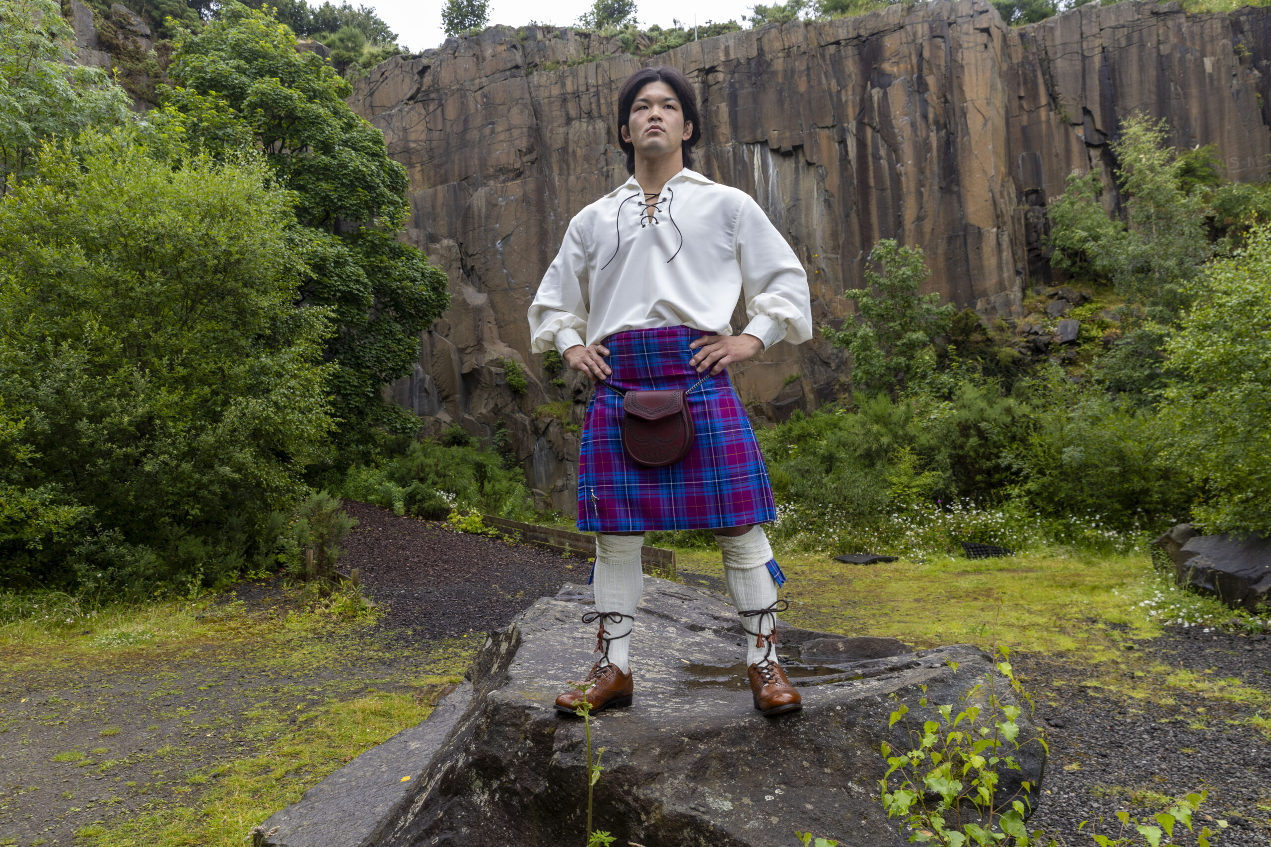 Ono standing on a rock in quarry wearing full Scottish Kilt outfit and JudoScotland kilt