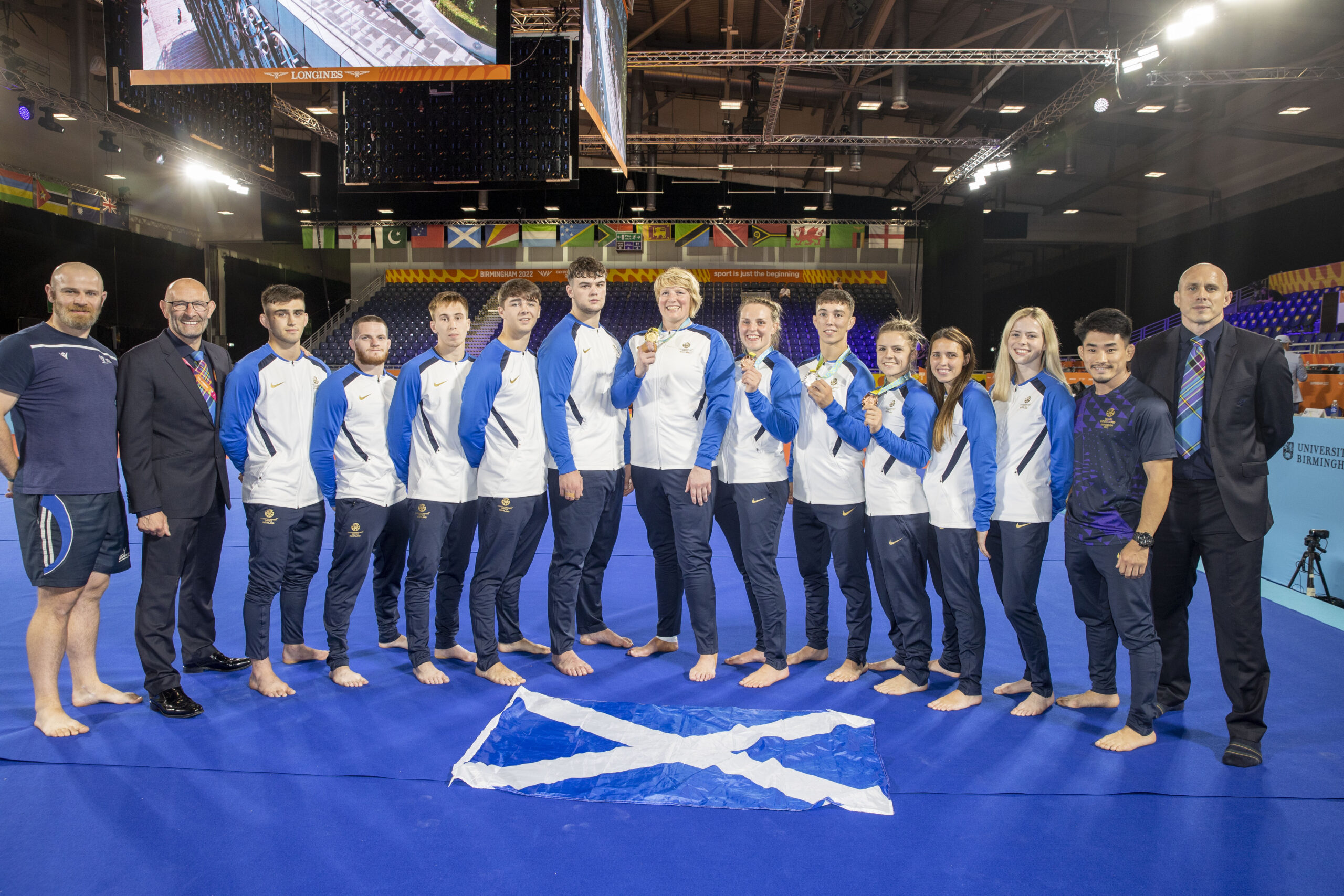 Team Scotland Judo at the Birmingham 2022 Commonwealth Games, The full team stands on the competition mat in full Team Scotland tracksuits. The 4 medal winners hold their medals proudly.