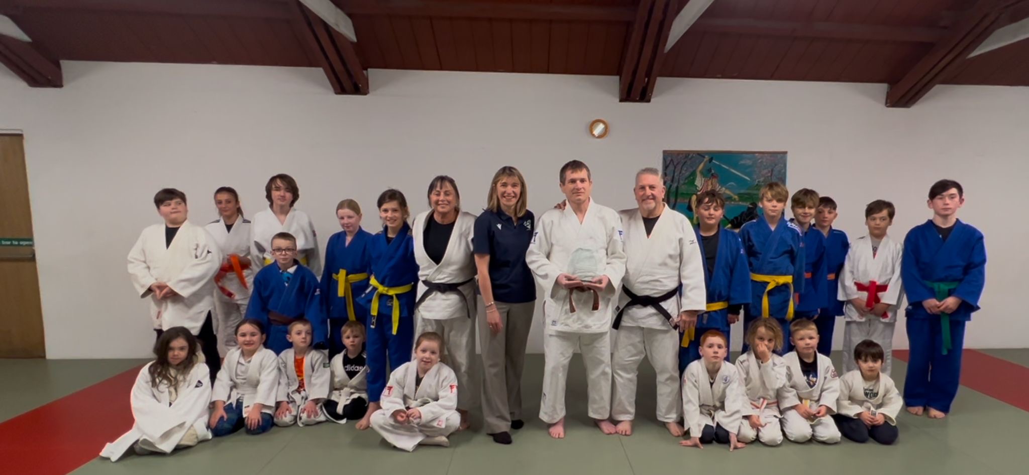 Chris is presented his award by JudoScotland CEO Judith McCleary at his club surrounded by the club members who nominated him.